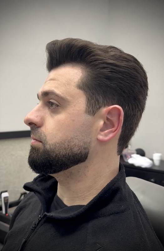 Homem com barba cheia, contorno bem definido e degradê nas laterais, feita na barbearia